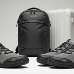 A pair of grey and black Xero Shoes—known as lightweight travel shoes—is placed in front of a black Xero backpack and a white hard-shell suitcase, all set against a neutral background.